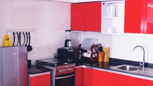 A kitchen with red cabinets, a stove, an oven, a sink, and various kitchen utensils. - Ivon Suites (Lagos)