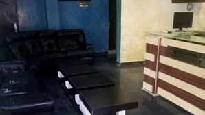 A reception area with a black leather sofa, a counter with a computer monitor, and a framed picture on the wall. - Seafortunes Royal Suites (Lagos)
