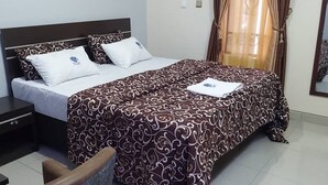 A neatly made bed with a patterned bedspread, a bedside table with a lamp, and a chair. - Seafortunes Royal Suites (Lagos)