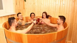 A group of people in a wooden hot tub with a window and a plant in the background. - Euro Beer Spa (Depoltovice)