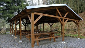 A wooden pavilion with picnic tables, set on a cobblestone surface, surrounded by trees. - Euro Beer Spa (Depoltovice)