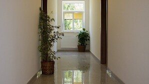 A hallway with a polished floor, a window with blinds, and potted plants. - Euro Beer Spa (Depoltovice)