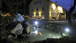 A building with a stone pathway leading to a pond, surrounded by trees and illuminated by warm lights. - Euro Beer Spa (Depoltovice)