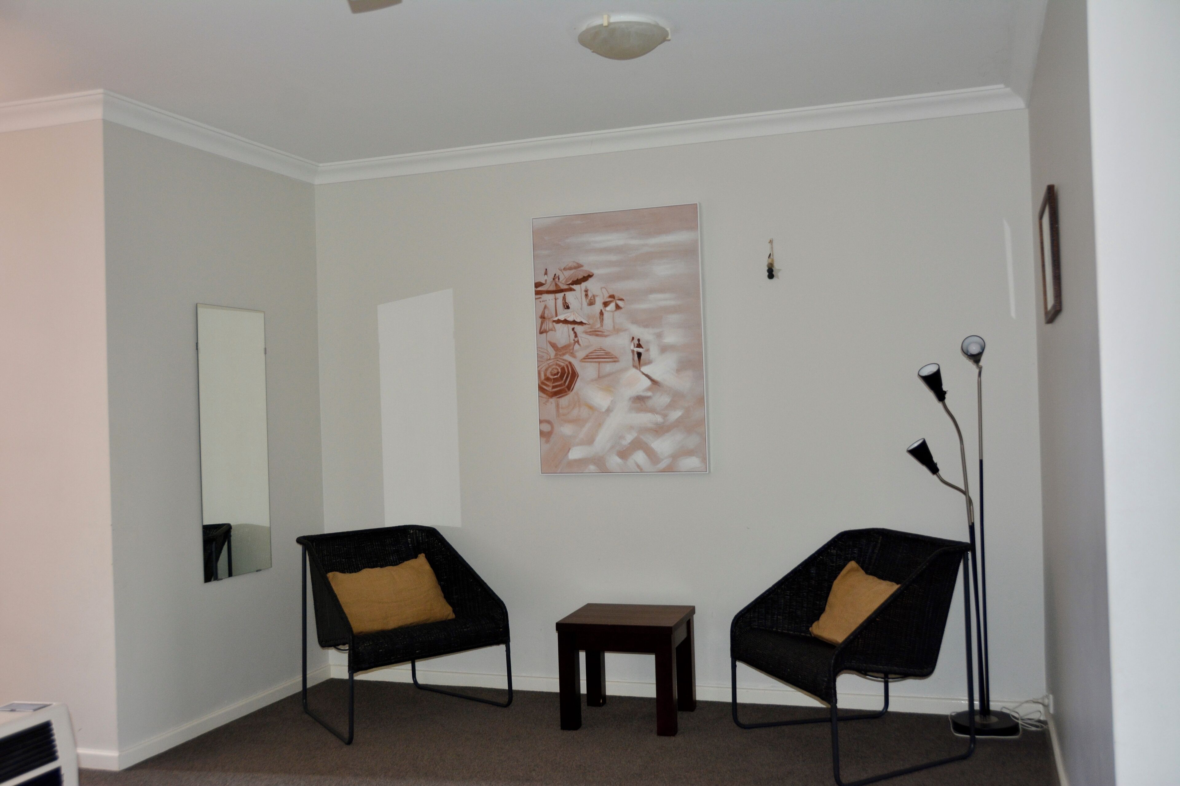 A room with two black chairs, a small table, a floor lamp, and a large abstract painting on the wall.
