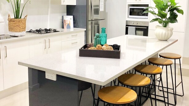 Una cocina moderna con una isla grande, taburetes de bar y dos plantas en macetas.