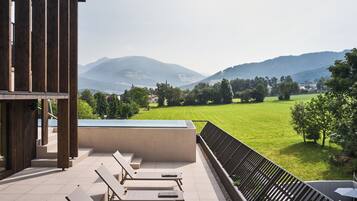 A terrace with lounge chairs, a view of a green field, and mountains in the distance.