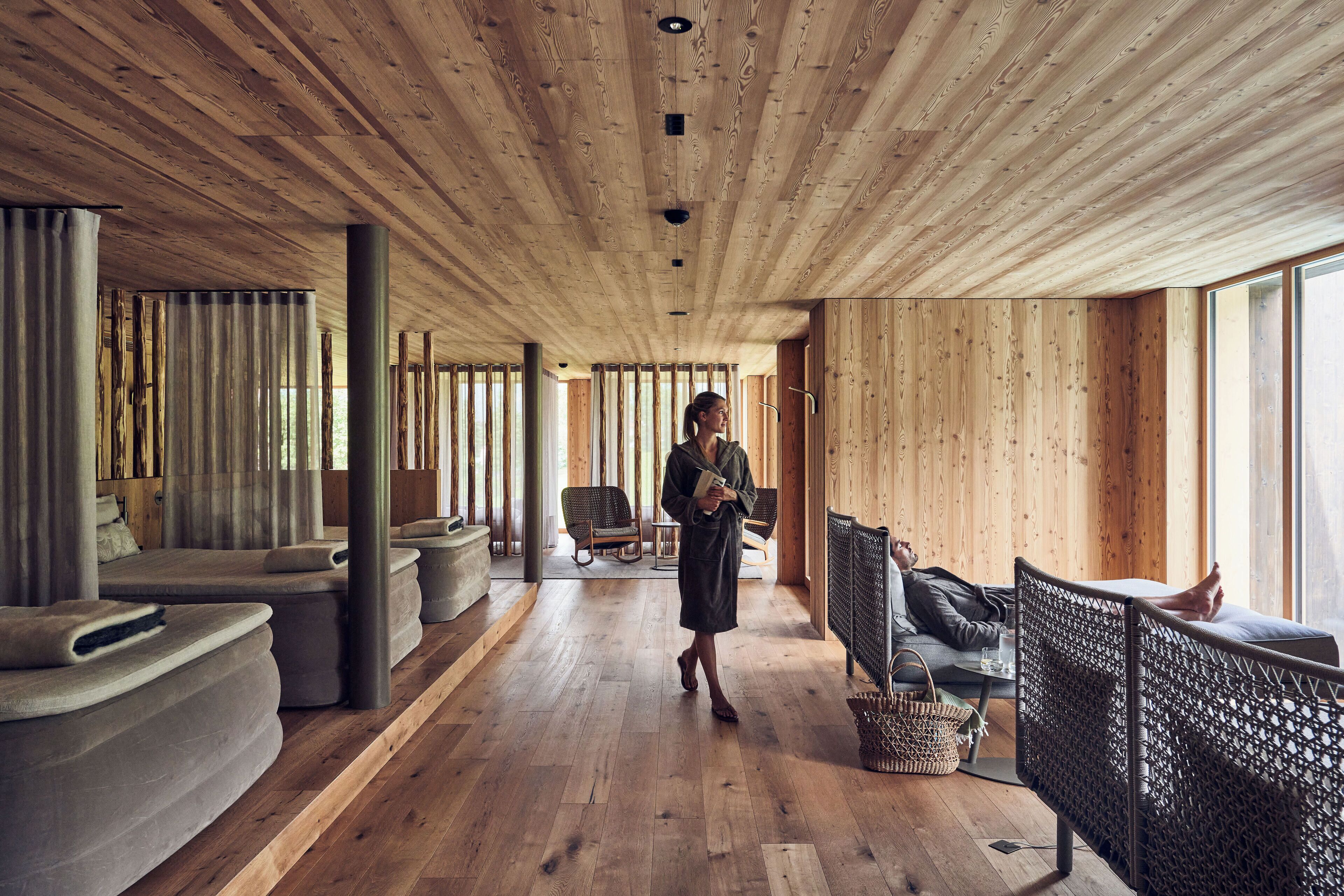 A spacious room with wooden floors and walls, featuring a sofa, chairs, and a reading area.