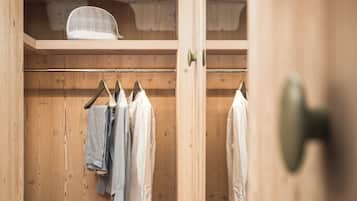 A wooden walk-in closet with hanging clothes and a shoe rack.