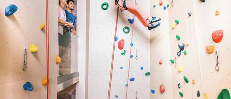 Una persona escalando una pared con puntos de agarre de colores, con una cuerda roja de seguridad.