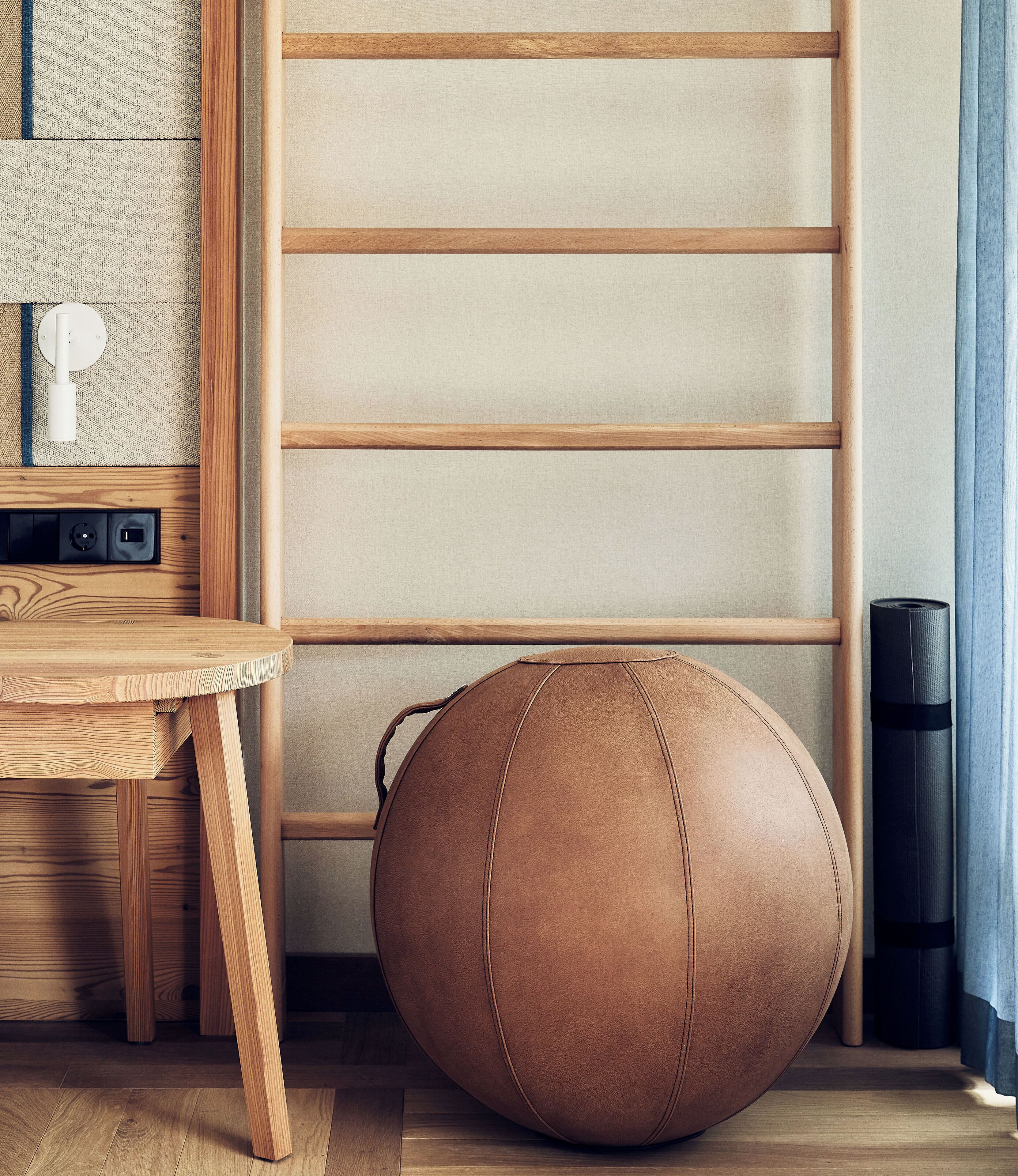 A room with a wooden floor, a round leather ottoman, a small wooden table, and a wall-mounted shelf with a power outlet.