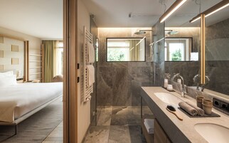 Una habitación de hotel moderna con una cama grande, un baño con ducha de vidrio y un tocador con espejo.