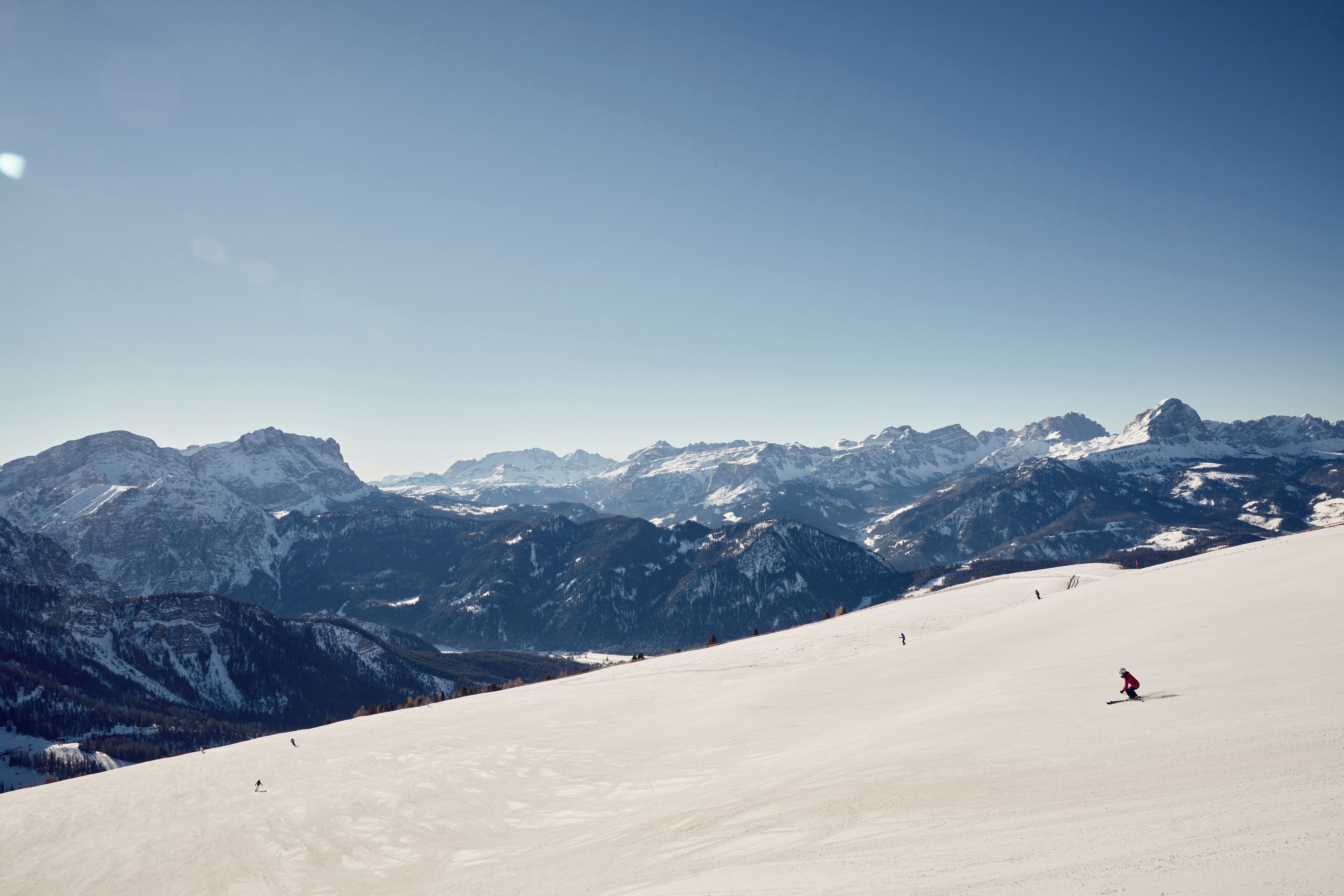 A snow-covered mountain slope with skiers and a clear sky.