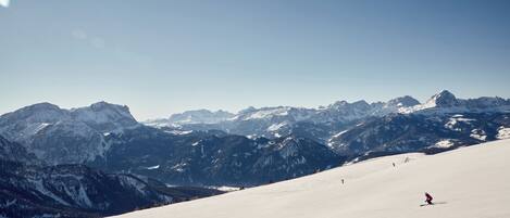 A snow-covered mountain slope with skiers and a clear sky.