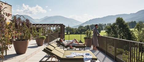 A balcony with lounge chairs, potted plants, and a view of mountains.