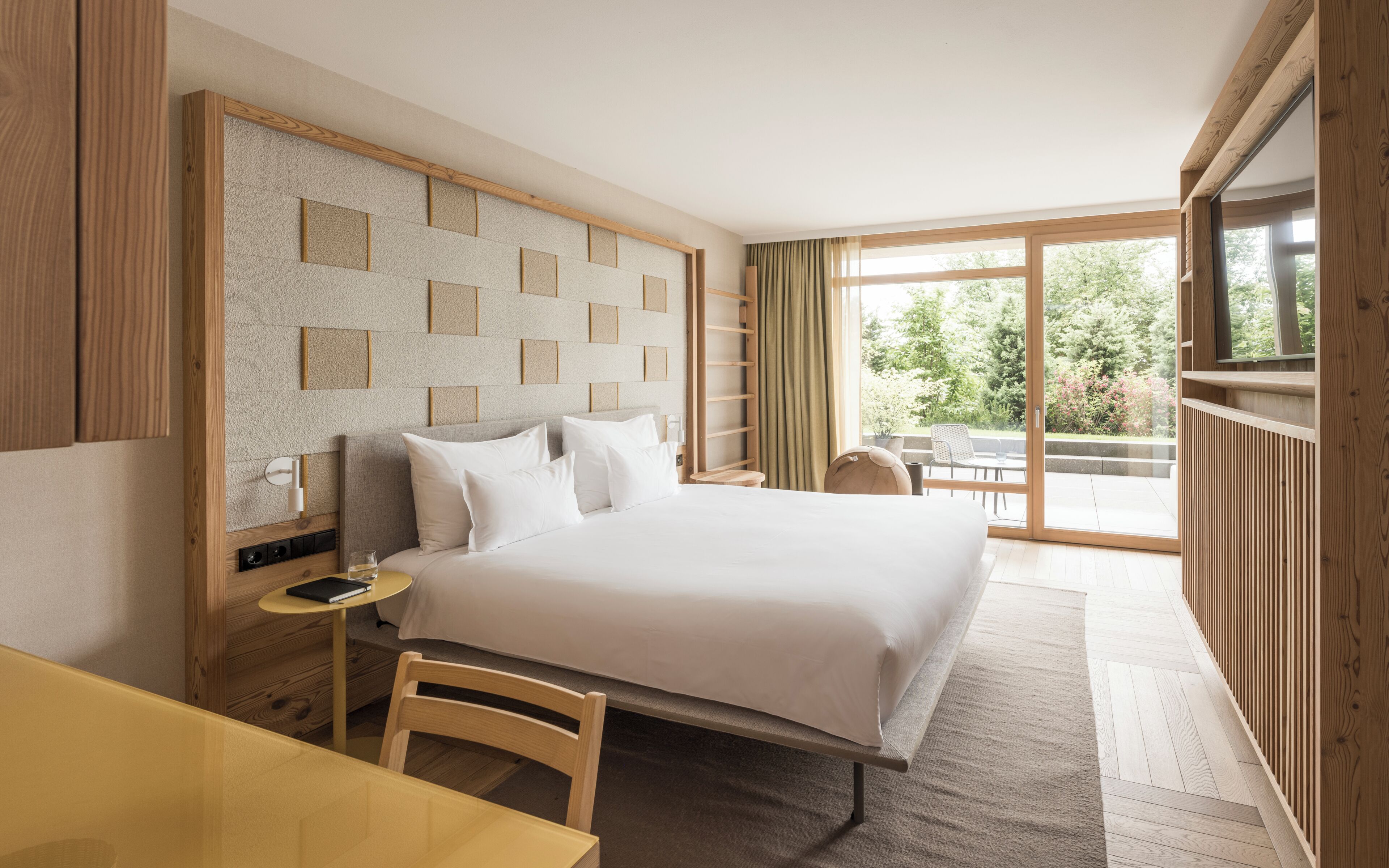 A hotel room with a large bed, a desk, a chair, and a view of the outdoors.
