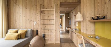 A modern interior with a wooden floor, a sofa with cushions, a chair, a small table, and a hanging light fixture.