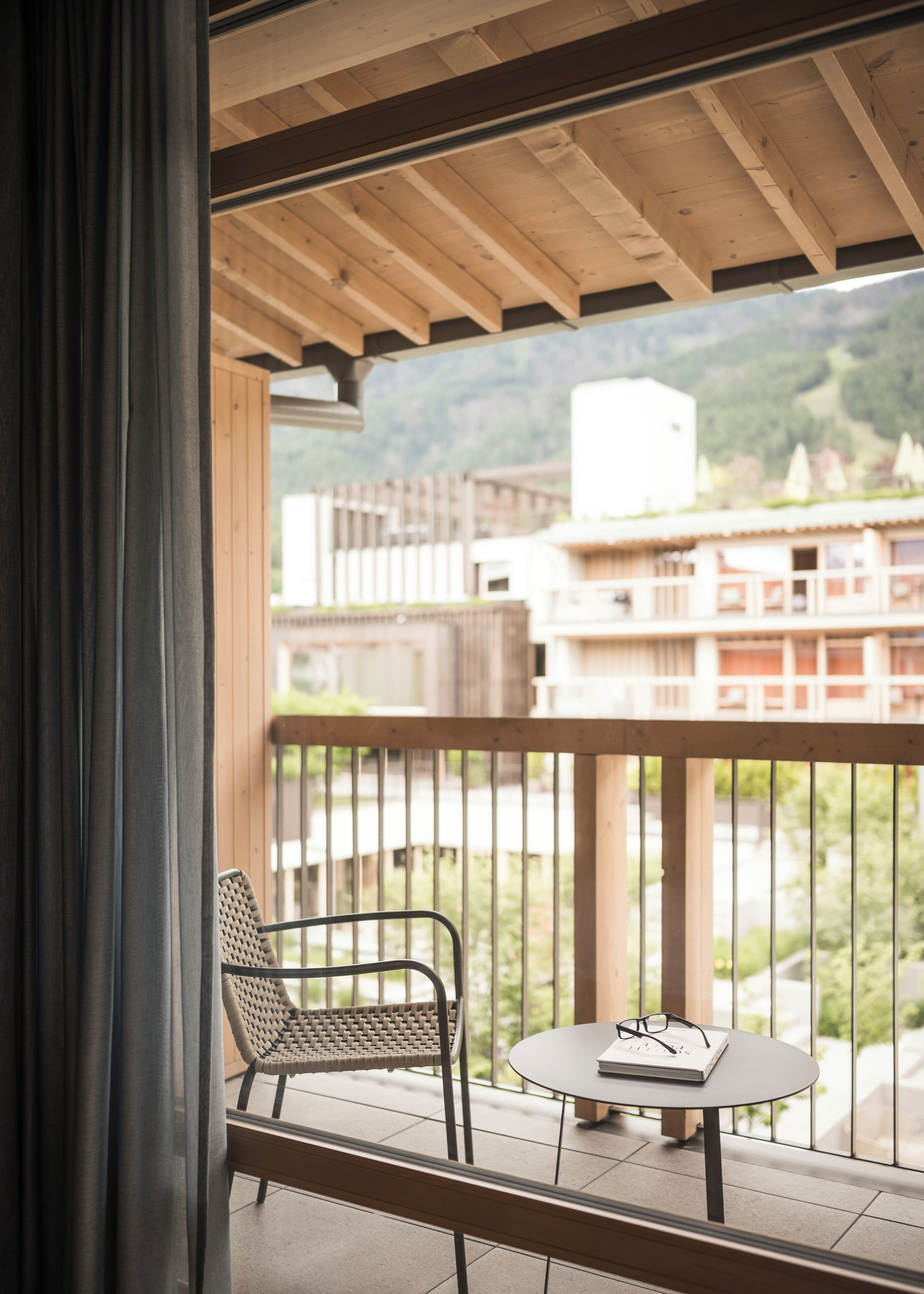 Un balcón con una silla y una mesita, con vistas a un edificio y una montaña.