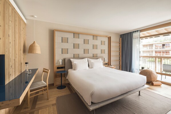 A modern hotel room with a large bed, a desk, and a view of the outside.