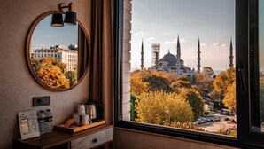 A hotel room with a large window offering a view of a mosque and autumn trees. - World Heritage Center Hotel (Istanbul)