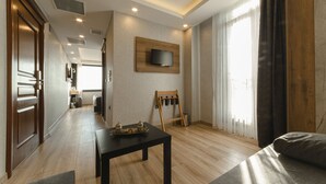 A modern hotel room with a wooden floor, a flat-screen TV mounted on the wall, a small table with a tray, and a large window with curtains. - World Heritage Center Hotel (Istanbul)