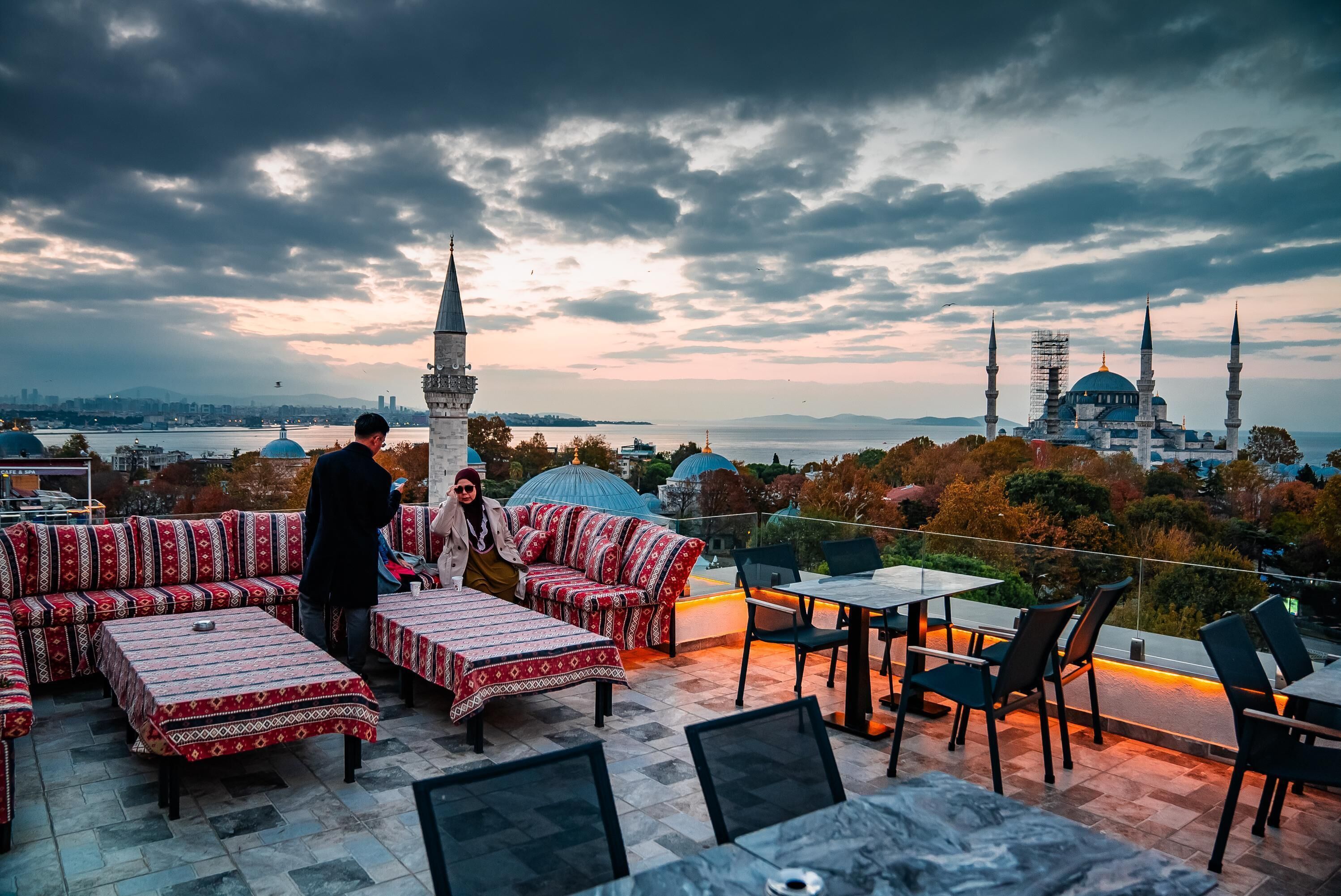 A rooftop terrace with outdoor seating, a view of a mosque, and a body of water in the background.
