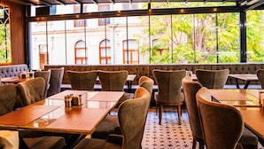 A restaurant with a modern interior, featuring wooden tables and cushioned booths, large windows with a view of buildings and trees, and a patterned floor. - World Heritage Center Hotel (Istanbul)