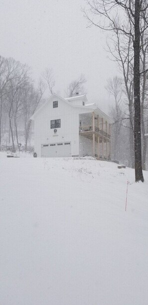 A white building with a garage, surrounded by trees and covered in snow. - Secluded, Cozy Cottage in the Shenandoah Valley (Maurertown)