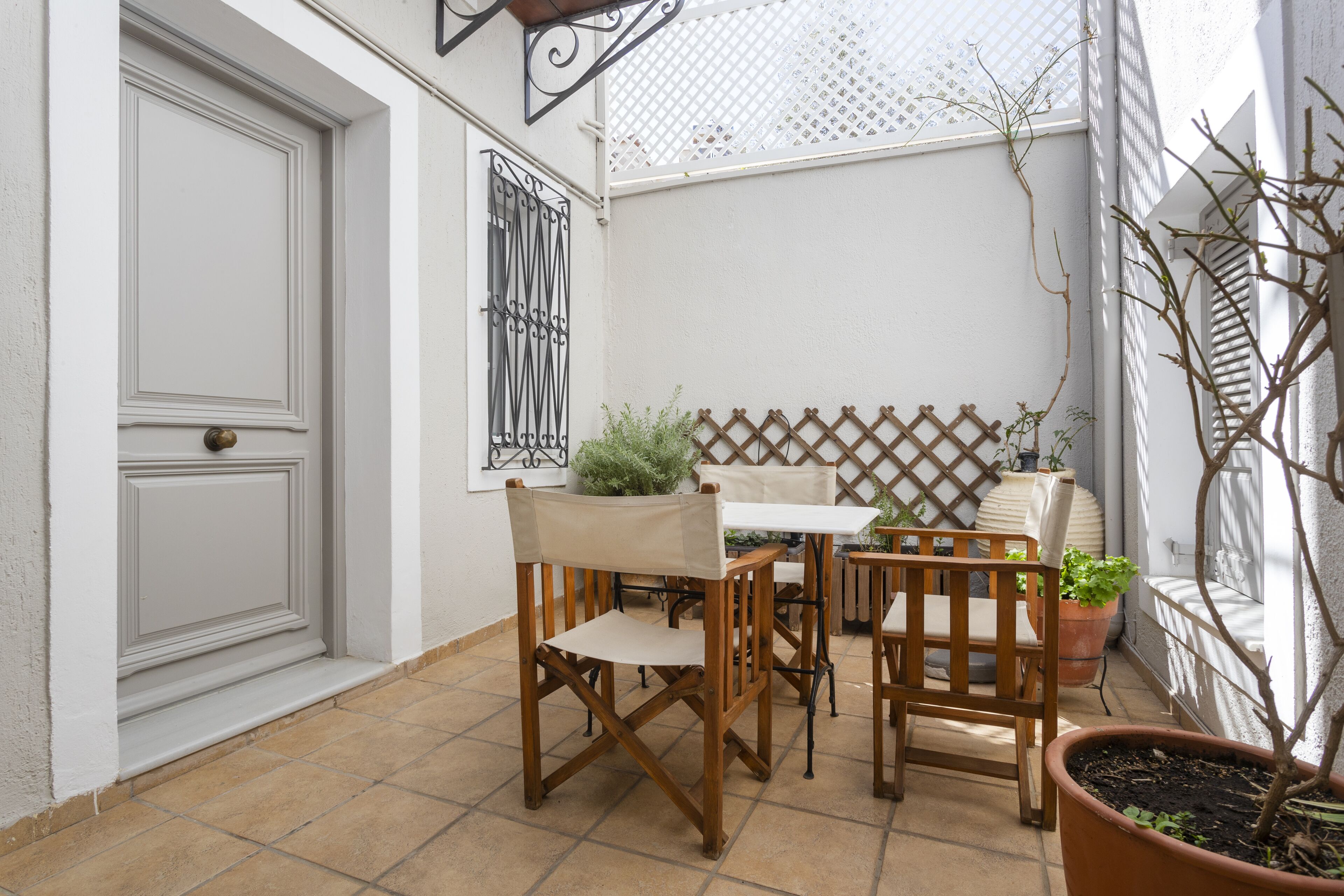 Un patio con una puerta blanca, una mesa con sillas y plantas en macetas.
