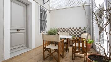 Un patio con una puerta blanca, una mesa con sillas y plantas en macetas.