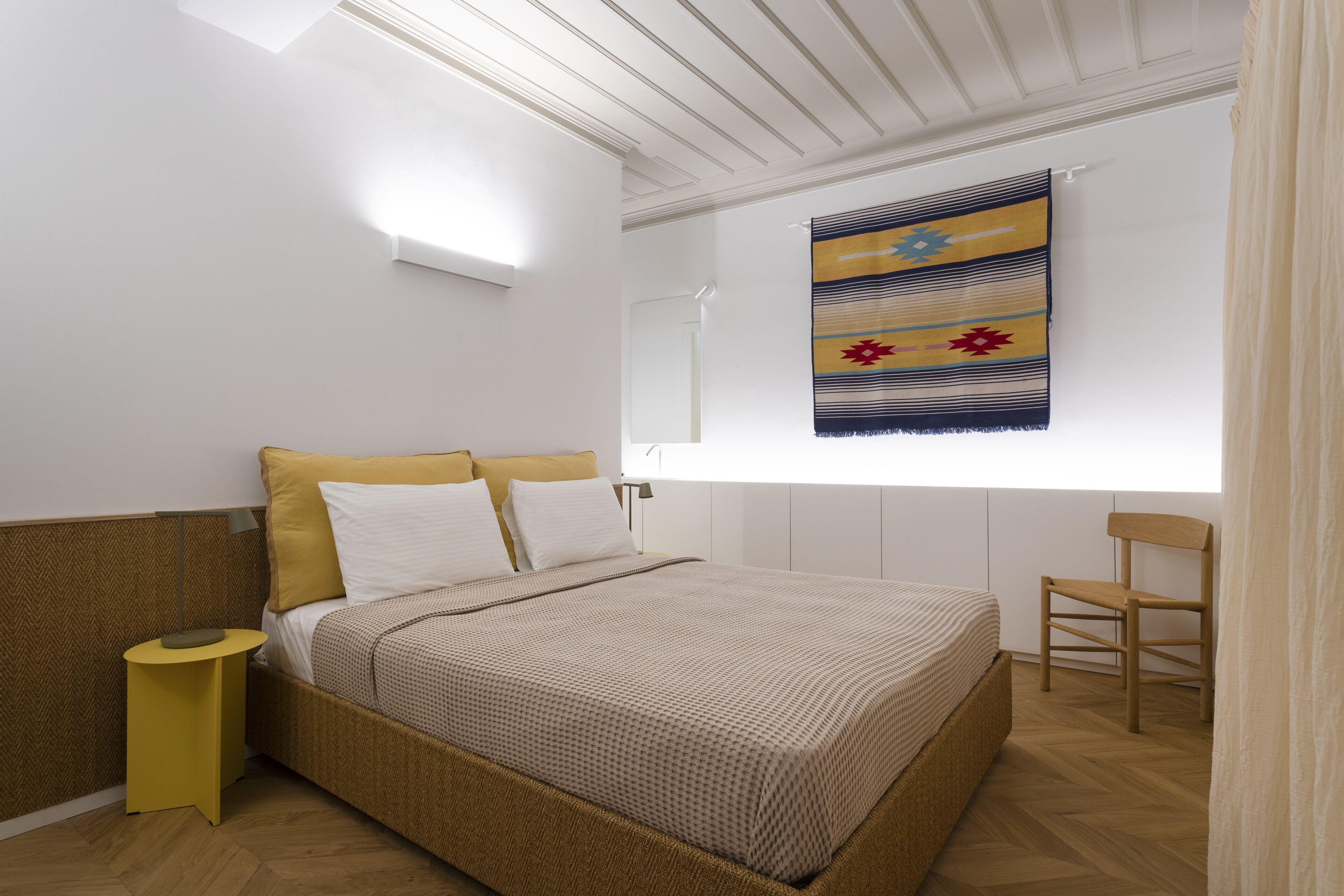Una camera da letto con un letto, un comodino, una sedia, una finestra vista e un'opera d'arte appesa al muro.