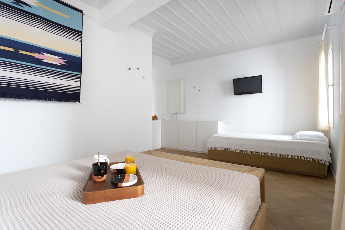 A hotel room with a bed, a bedside table with a tray of breakfast, a television, and a window with curtains.