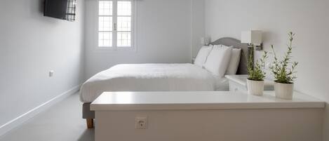 A minimalist bedroom with a bed, bedside tables, a TV, and two potted plants.