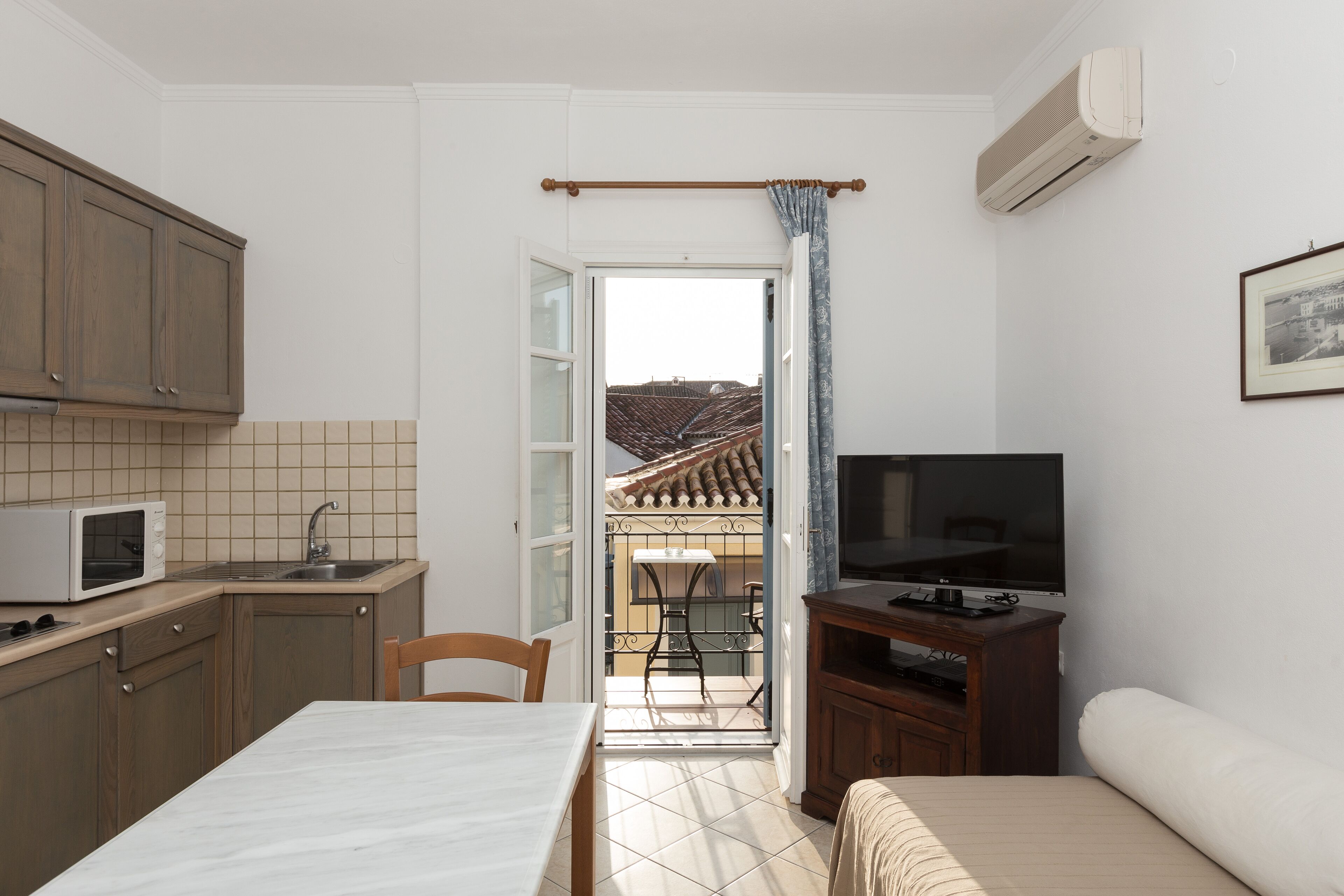 A compact room with a kitchenette, a dining area, a bed, and a TV.