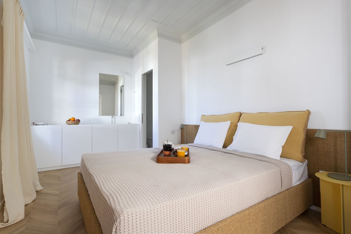A neatly arranged bedroom with a bed, bedside table, and a small table with a tray of breakfast items.