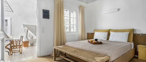 Un dormitorio con cama, mesita de noche, banco y vistas a un balcón.