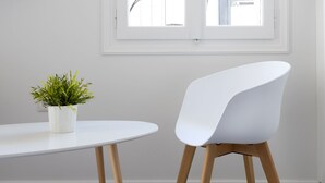Une pièce avec une table blanche, une chaise blanche, une plante en pot et une fenêtre avec un store blanc.