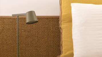 A bed with a mustard-colored pillow and a white pillow, a round yellow nightstand with a lamp, and a herringbone-patterned wall.