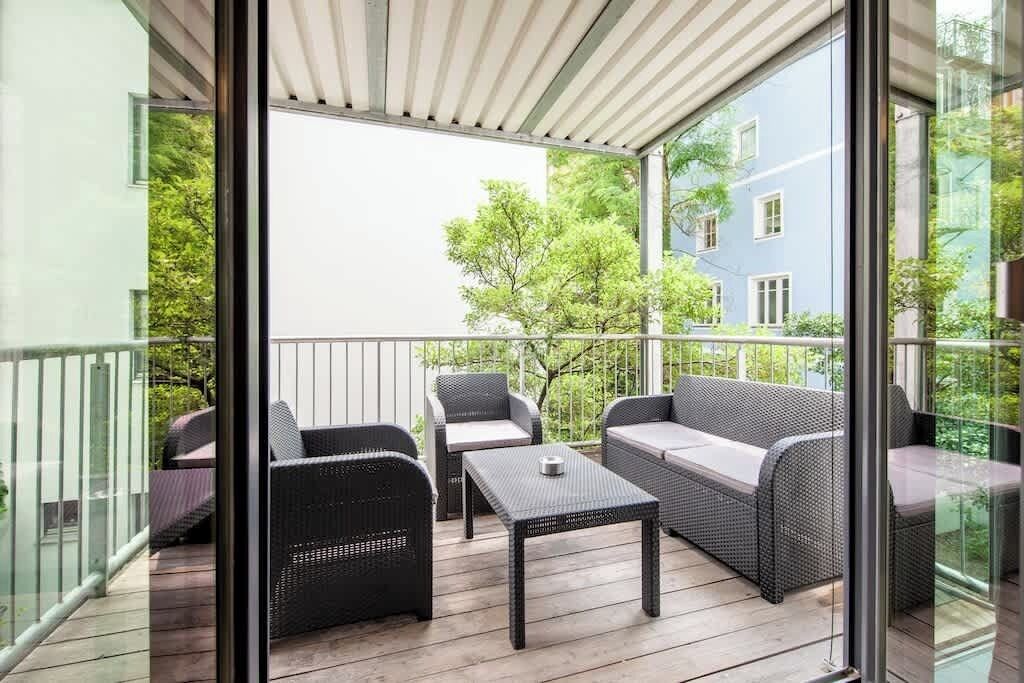 Un balcon agrémenté de meubles en osier, d’une table et offrant une vue sur un immeuble et des arbres.