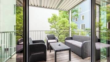 Un balcon agrémenté de meubles en osier, d’une table et offrant une vue sur un immeuble et des arbres.