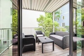 A balcony with wicker furniture, a table, and a view of a building and trees.