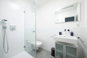 Ein modernes Badezimmer mit Duschkabine aus Glas, Toilette, Waschbecken mit Spiegel und einem Schrank.