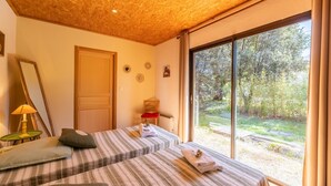 A room with two beds, a wooden ceiling, a large window, and a door.