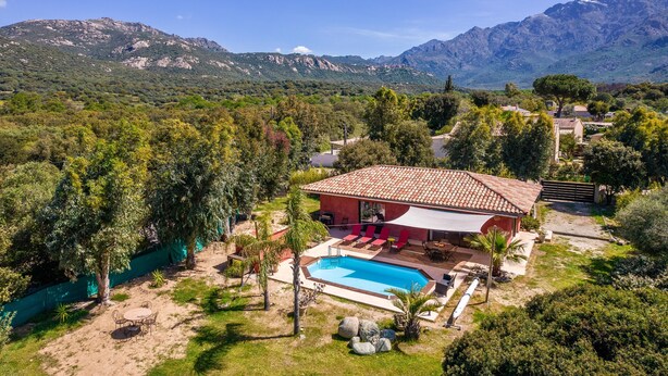 A villa with a swimming pool, surrounded by lush greenery and mountains in the background.