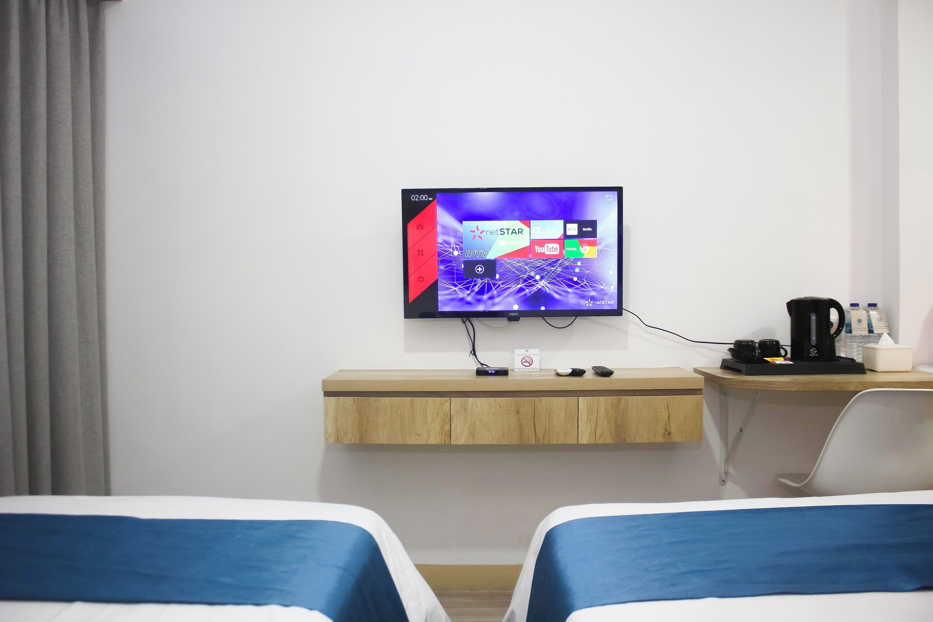 A hotel room with two beds, a TV mounted on the wall, a wooden desk, a coffee maker, and a remote control.
