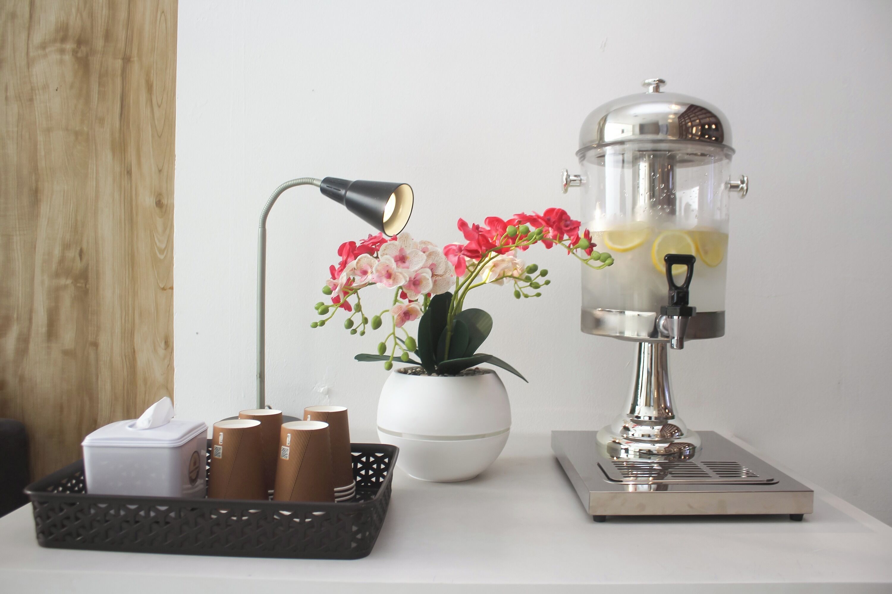 A coffee machine, a lamp, a plant, and a basket with cups on a table.