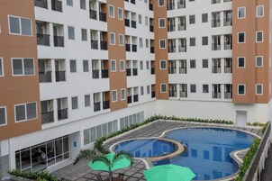 Um edifício residencial de vários andares com um pátio central que apresenta uma piscina, rodeado por varandas e janelas.