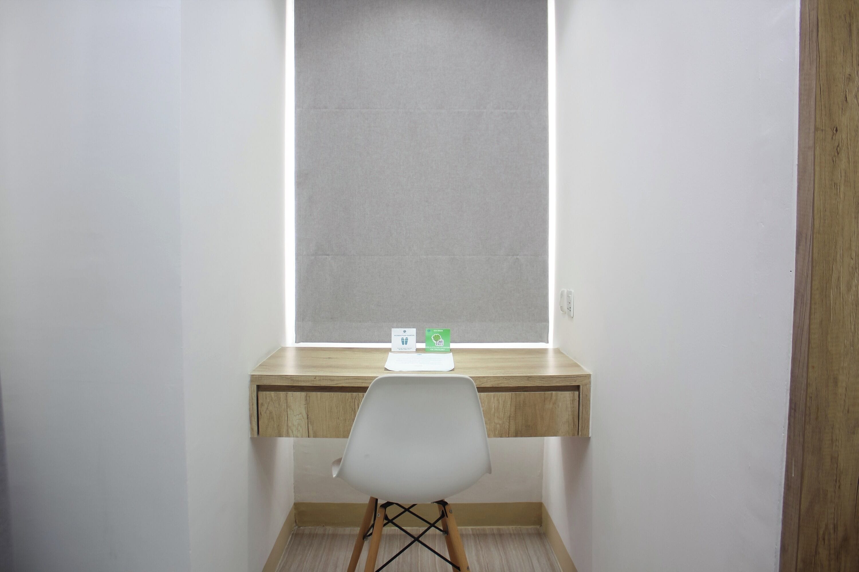 Ein kleiner, privater Arbeitsraum mit einem Holztisch, einem weißen Stuhl und einem Fenster mit Jalousien.