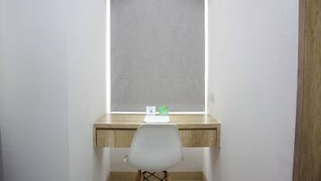 Ein kleiner, privater Arbeitsraum mit einem Holztisch, einem weißen Stuhl und einem Fenster mit Jalousien.