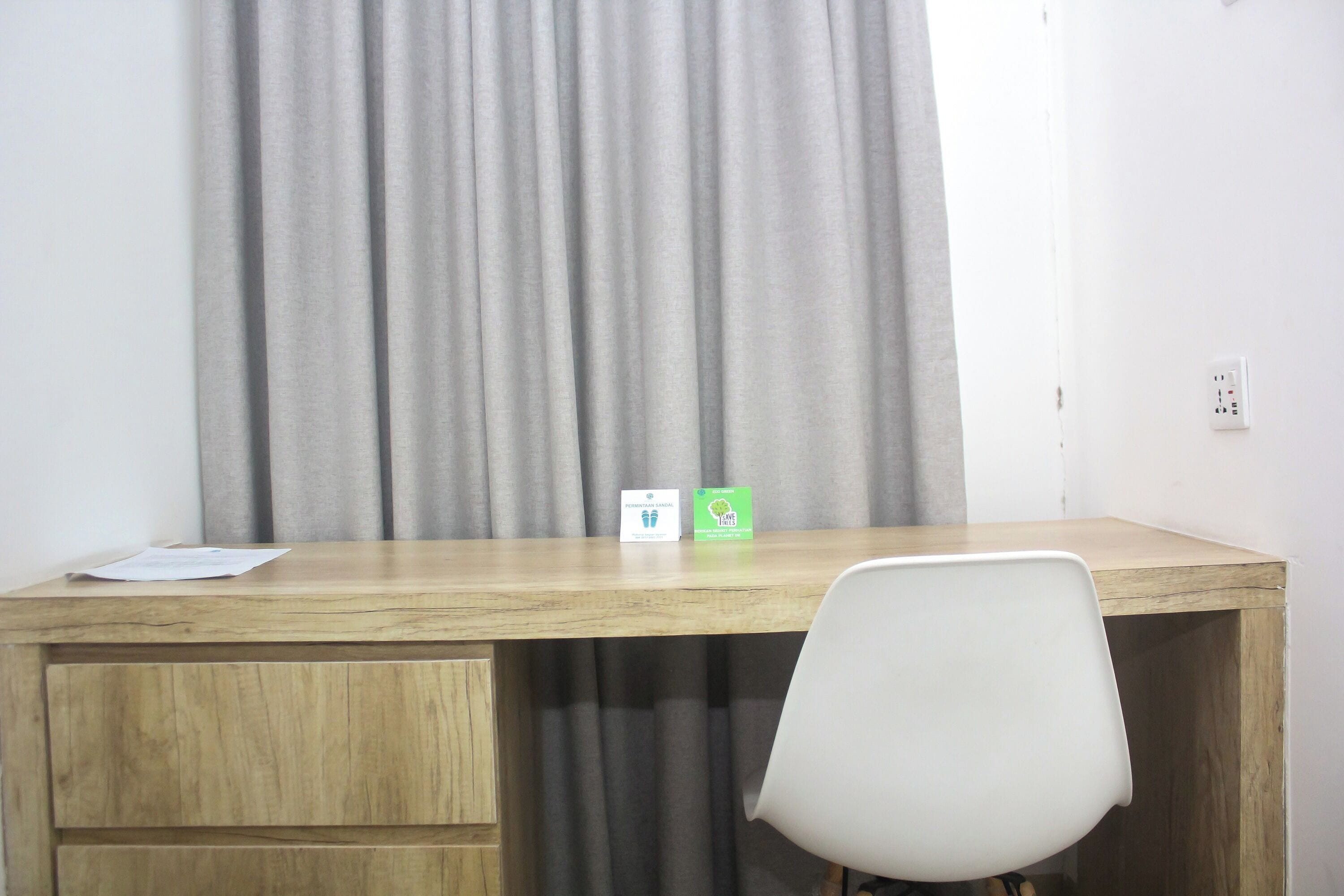 Un bureau en bois, une chaise blanche, un rideau et deux panneaux accrochés au mur.