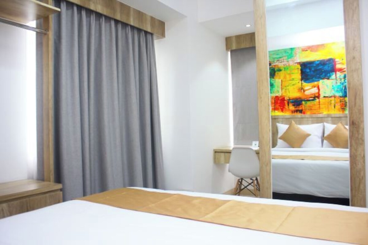 A hotel room with a bed, a desk, a chair, and a large mirror reflecting a colorful painting.